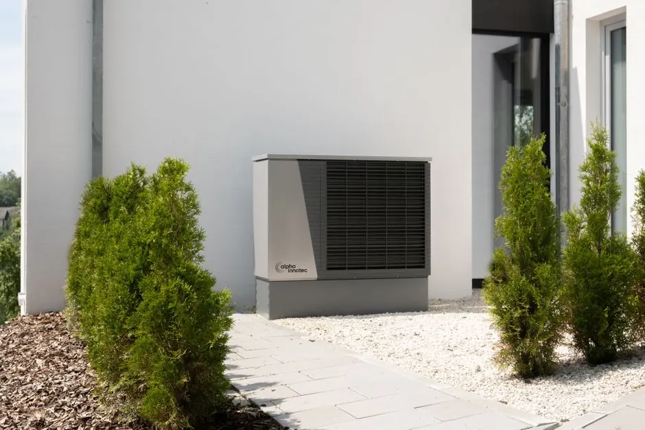 Outdoor air conditioner unit on a modern building surrounded by greenery and landscaping.
